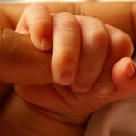 Doesn't let go: baby holding onto adult finger.